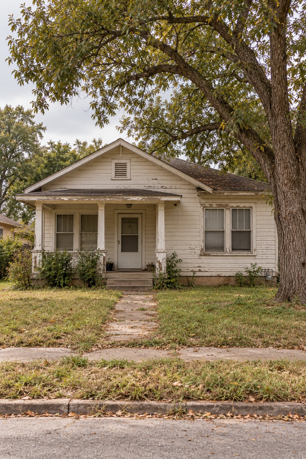 A modest wood-sided bungalow with peeling trim and a small front porch